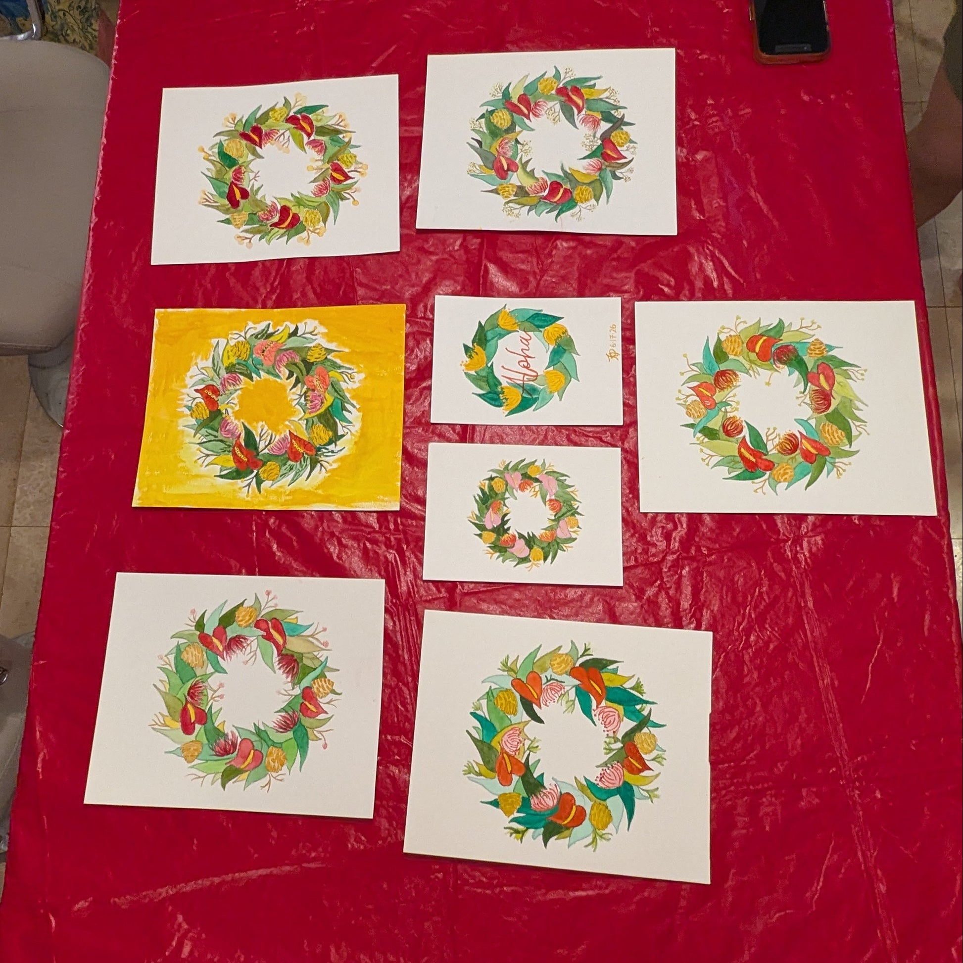 Colorful wreath designs on white paper laid out on a red tablecloth.